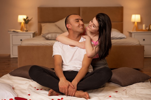 Mężczyzna i kobieta siedzą na podłodze w sypialni, obejmując się ramionami