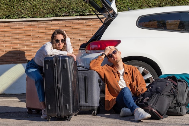 Zdjęcie mężczyzna i kobieta siedzą na podłodze zmęczeni i zdesperowani z bagażem w bagażniku samochodu