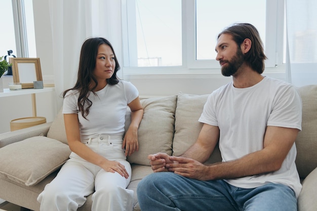 Mężczyzna i kobieta siedzą w domu na kanapie w białych stylowych koszulkach i rozmawiają wesoło uśmiechając się i śmiejąc się w domu Przyjaźń mężczyzn i kobiet