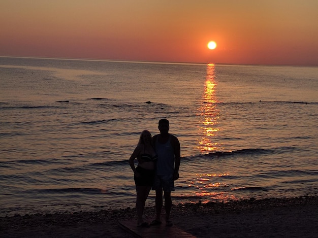 Mężczyzna i kobieta stojący na plaży na tle nieba podczas zachodu słońca