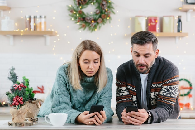 Mężczyzna i kobieta w domu oglądający telefony komórkowe spędzający czas na portalach społecznościowych, Boże Narodzenie i Nowy Rok