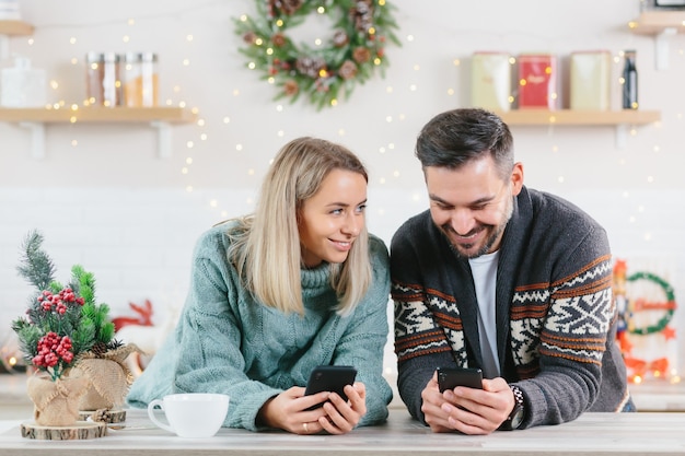 Mężczyzna i kobieta w domu oglądający telefony komórkowe spędzający czas na portalach społecznościowych, Boże Narodzenie i Nowy Rok