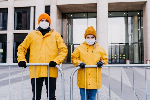 Mężczyzna i kobieta w maskach chirurgicznych stojących za płotem podczas kwarantanny, czekających na pomoc ze strony rządu lub ludzi. Blokada podczas koncepcji pandemii covida-19.