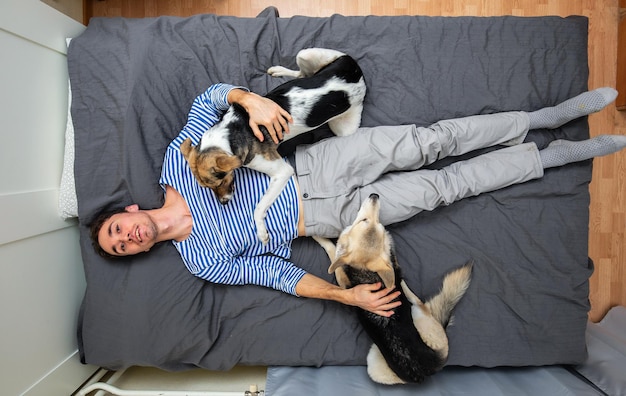 Mężczyzna i psy leżące na łóżku z szarym prześcieradłem