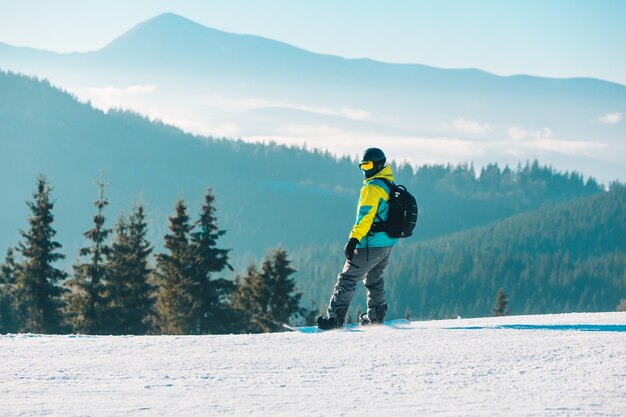 Mężczyzna idący przez wzgórze z górami snowboardowymi w tle