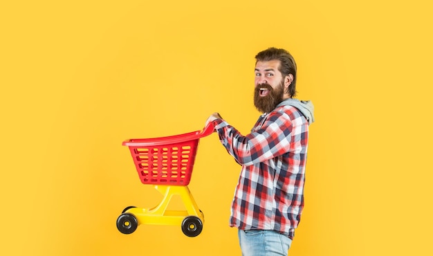 Mężczyzna idzie na zakupy śmieszny mężczyzna z małym wózkiem weekend na kupowanie produktów raduje się z udanych zakupów brutalny dojrzały hipster idzie na zakupy Czas napełnić koszyk