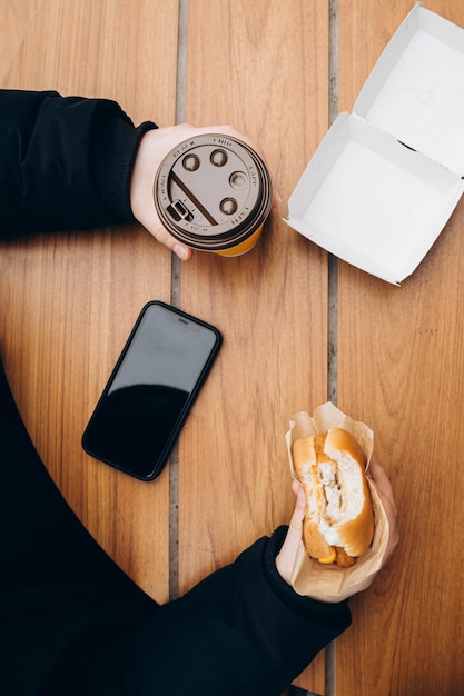 Mężczyzna je hamburgera i pije kawę siedząc przy stole w kawiarni z fast foodem