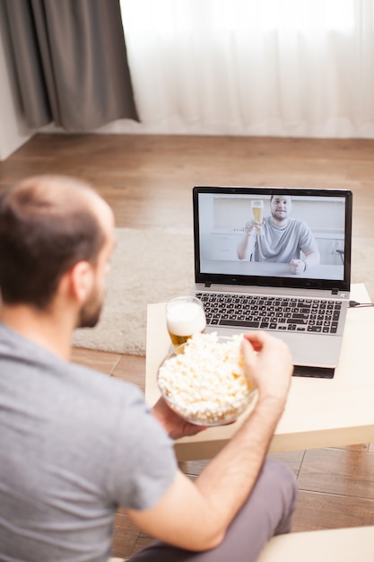 Mężczyzna je popcorn podczas rozmowy wideo ze swoim przyjacielem podczas samoizolacji.