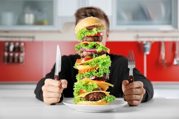 Mężczyzna jedzący ogromnego burgera przy stole