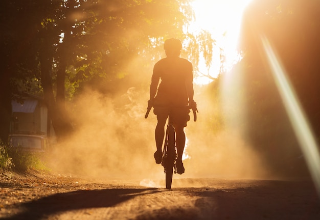 Zdjęcie mężczyzna jedzie na rowerze na żwirowej drodze o zachodzie słońca. sylwetka rowerzysty na rowerze szutrowym w chmurze pyłu.