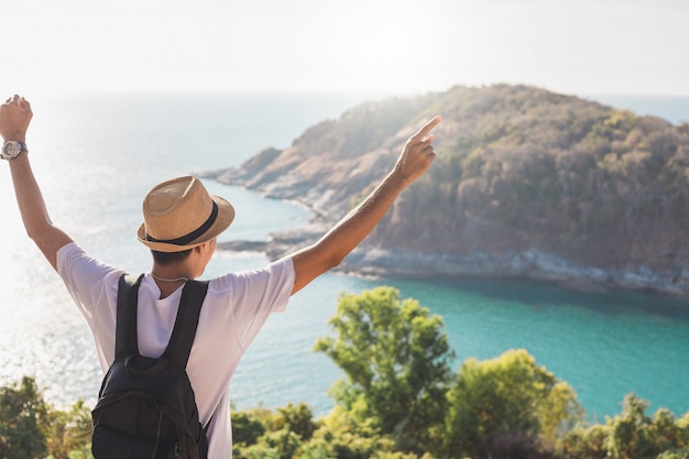 Mężczyzna jest ubranym kapelusz trzyma jego rękę szczęśliwą. Mężczyzna azjatycki turysta Spójrz na góry i morze Przed zachodem słońca. Dla aktywności styl życia na zewnątrz wolność lub podróż turystyka inspiracja backpacker turysta covid 19