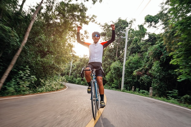Zdjęcie mężczyzna jeździ na rowerze na drodze. człowiek, jazda rowerem sportowym vintage na wieczorne ćwiczenia. mężczyzna jeździ na rowerze, aby odetchnąć świeżym powietrzem pośród natury, łąki, lasu, przez które prześwituje wieczorne słońce