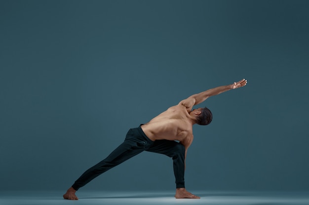 Mężczyzna joga robi ćwiczenia rozciągające w studio, szara ściana Siłacz uprawiający jogina, trening asan, najwyższa koncentracja, zdrowy tryb życia