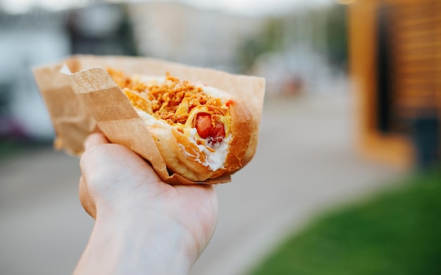 Mężczyzna kaukaski ręka trzyma świeżego hot doga ze smażoną cebulą fast food na zewnątrz zbliżenie selektywne skupienie się na kiełbasie