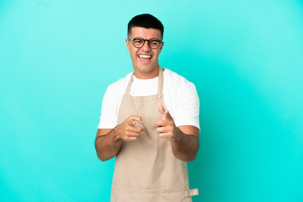 Mężczyzna kelner w restauracji na odosobnionym niebieskim tle, wskazując do przodu i uśmiechnięty