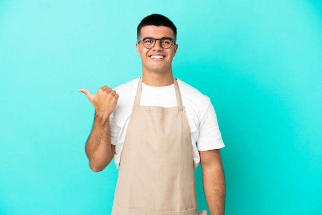 Mężczyzna kelner w restauracji na odosobnionym niebieskim tle, wskazując na bok, aby zaprezentować produkt