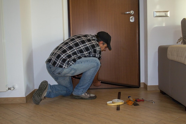 Mężczyzna klęczy na podłodze obok drzwi z napisem „naprawa”.