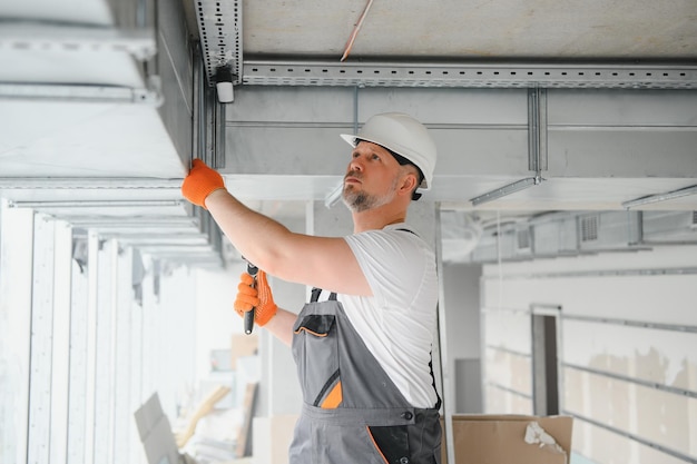Mężczyzna konfigurujący system wentylacji w pomieszczeniu Pracownik płci męskiej instaluje rury wentylacyjne w nowym biurowcu