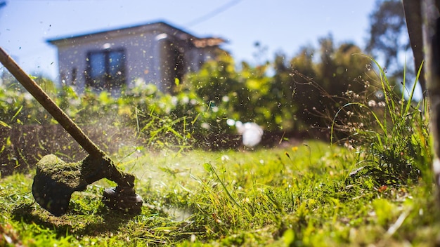 Mężczyzna koszący wysoką trawę za pomocą elektrycznej lub benzynowej przycinarki do trawy na podwórku Narzędzia i sprzęt do pielęgnacji ogrodów Proces przycinania trawnika za pomocą kosiarki ręcznej