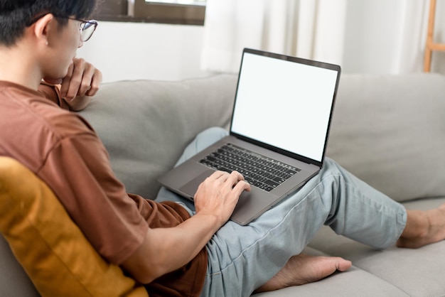 Mężczyzna, który zakłada okulary, opierając się plecami o ciemnożółty, skupiając się na laptopie