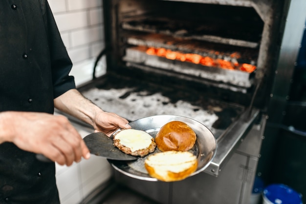 Mężczyzna kucharz przygotowuje smaczne mięso na grill piekarnik, gotowanie burger.