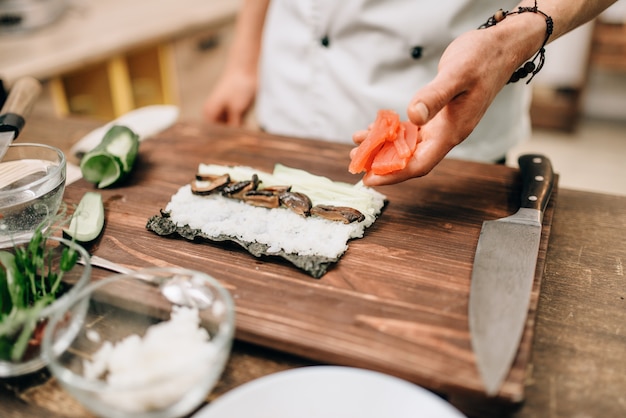 Mężczyzna kucharz robi sushi na drewnianym stole