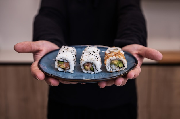 mężczyzna kucharz trzyma niebieski talerz Sushi Roll w kuchni.