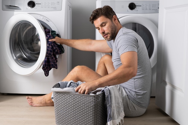 Mężczyzna ładowanie ubrań do pralki w pralni Mężczyzna w średnim wieku oddanie prania do prania
