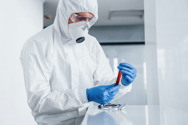 Mężczyzna lekarz naukowiec w fartuchu, okulary ochronne i maska trzyma probówki z krwią