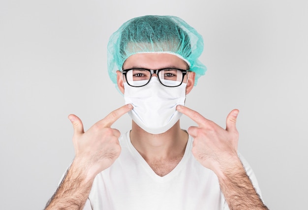 Mężczyzna lekarz w mundurze medycznym wskazuje palcami na maskę medyczną na twarzy