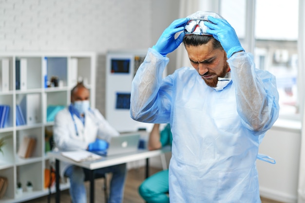 Mężczyzna lekarz w ochronnej sukni medycznej stojącej w gabinecie szpitalnym