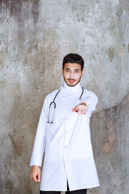 Mężczyzna lekarz ze stetoskopem stojąc na betonowej ścianie i pokazując osobę z przodu.