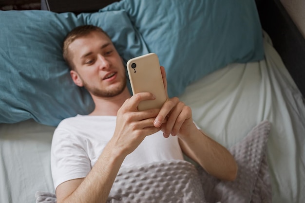 Mężczyzna leżący w łóżku trzymający telefon