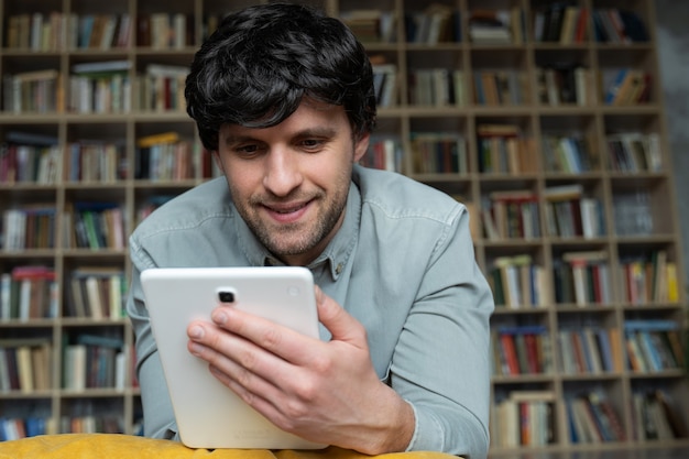 Mężczyzna leży na podłodze przy użyciu komputera typu tablet w domu na półce z książkami