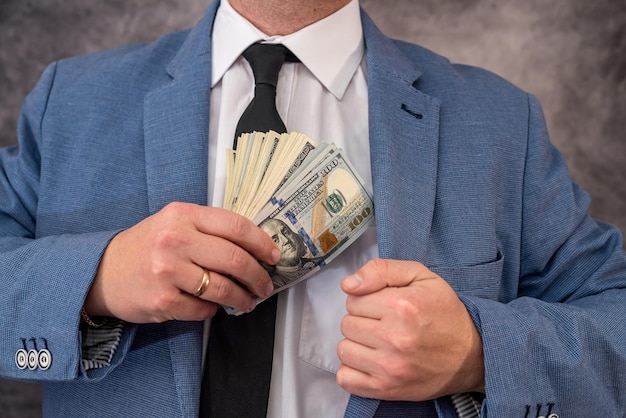 Mężczyzna lub funkcjonariusz w garniturze wkłada do kieszeni łapówkę w postaci banknotów studolarowych