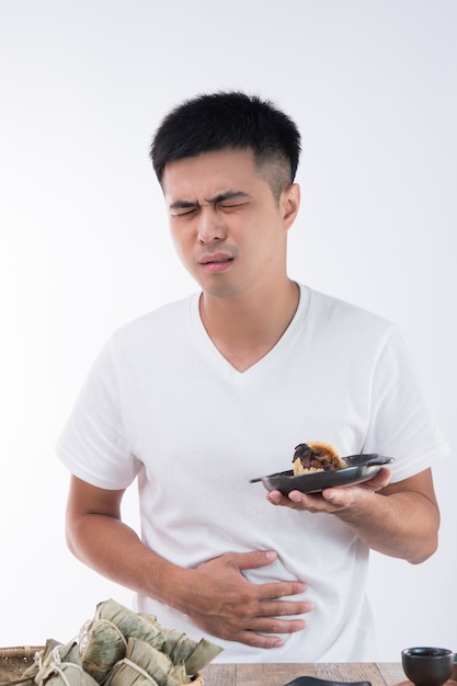 Mężczyzna ma ból brzucha po zjedzeniu pysznego zongzi (kluski ryżowej) na Dragon Boat Festival, azjatyckie tradycyjne jedzenie, białe tło