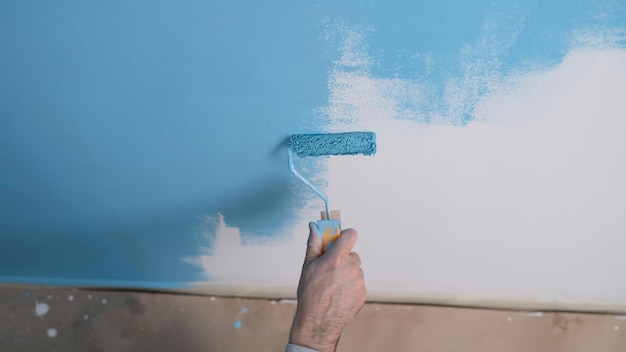 Mężczyzna maluje białą ścianę niebieskim barwnikiem w zbliżeniu