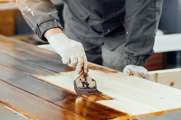 Mężczyzna maluje drewniane deski pędzlem Stolarz stolarz lakieruje powierzchnię drewnianą Autentyczny przepływ pracy