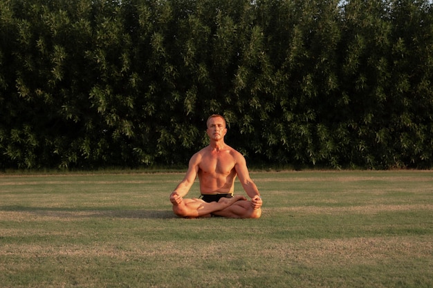 Mężczyzna medytuje w pozie padmasana jogi na trawie w ogrodzie oświetlonym złotym światłem słonecznym