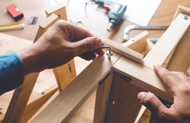 Mężczyzna montuje drewniane meble, mocuje lub naprawia dom za pomocą śrubokręta.