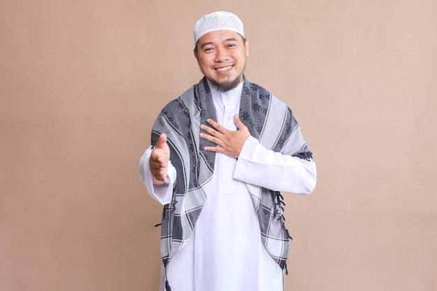 Mężczyzna muzułmański z Azji uśmiecha się przyjaźnie, oferując uścisk ręki na beżowym tle