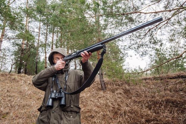 Mężczyzna myśliwy z lornetką gotowy do polowania, trzymając pistolet i spacerując po lesie