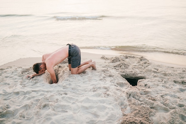 Mężczyzna na plaży kopanie dziury w piasku za morzem w lecie.