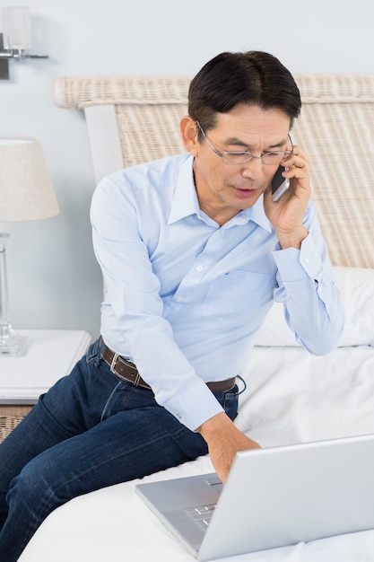 Mężczyzna Na Rozmowie Telefonicznej Używa Laptop W Sypialni