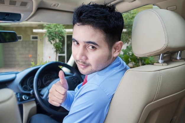 Mężczyzna na siedzeniu kierowcy patrzy wstecz i pokazuje kciuk.