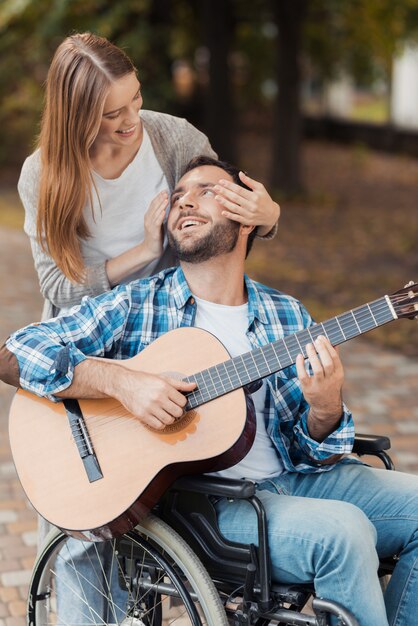 Mężczyzna na wózku inwalidzkim gra na gitarze w parku.