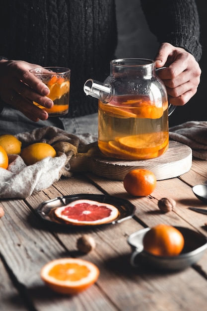 Mężczyzna nalewa herbatę cytrusową na drewniany stół. Zdrowy napój w stylu vintage. Wegańskie, ekologiczne produkty.