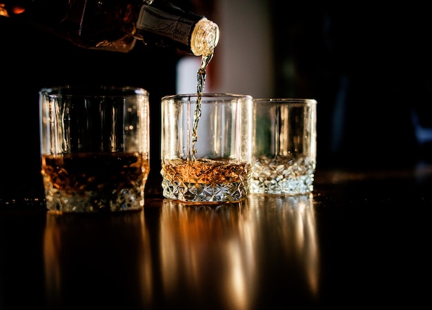 Mężczyzna nalewa whisky w szkłach stoi przed drewnianym stołem
