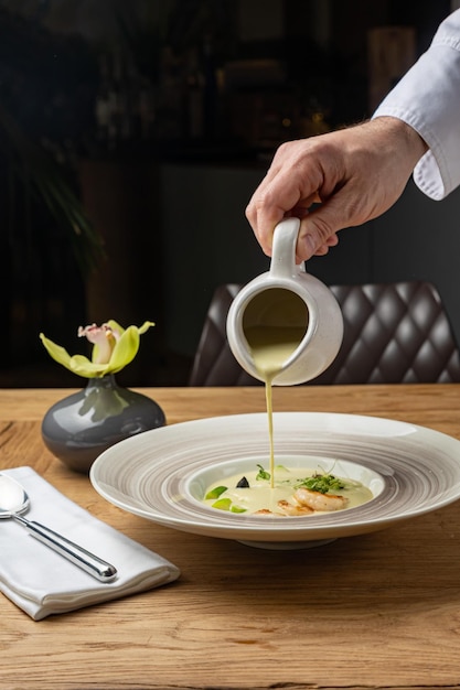 Mężczyzna nalewa zupę z miski na stole.