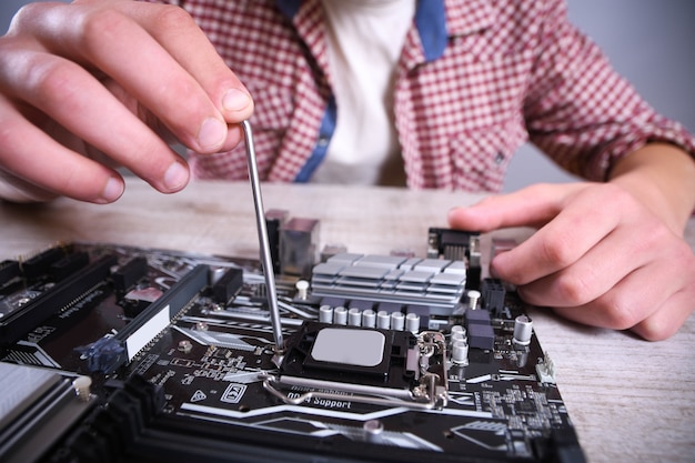 Mężczyzna naprawia zepsuty komputer, kartę graficzną, pamięć RAM, chłodnicę, procesor, dysk twardy. Młody serwisant pracujący z wkrętakiem w centrum serwisowym. Nastolatek